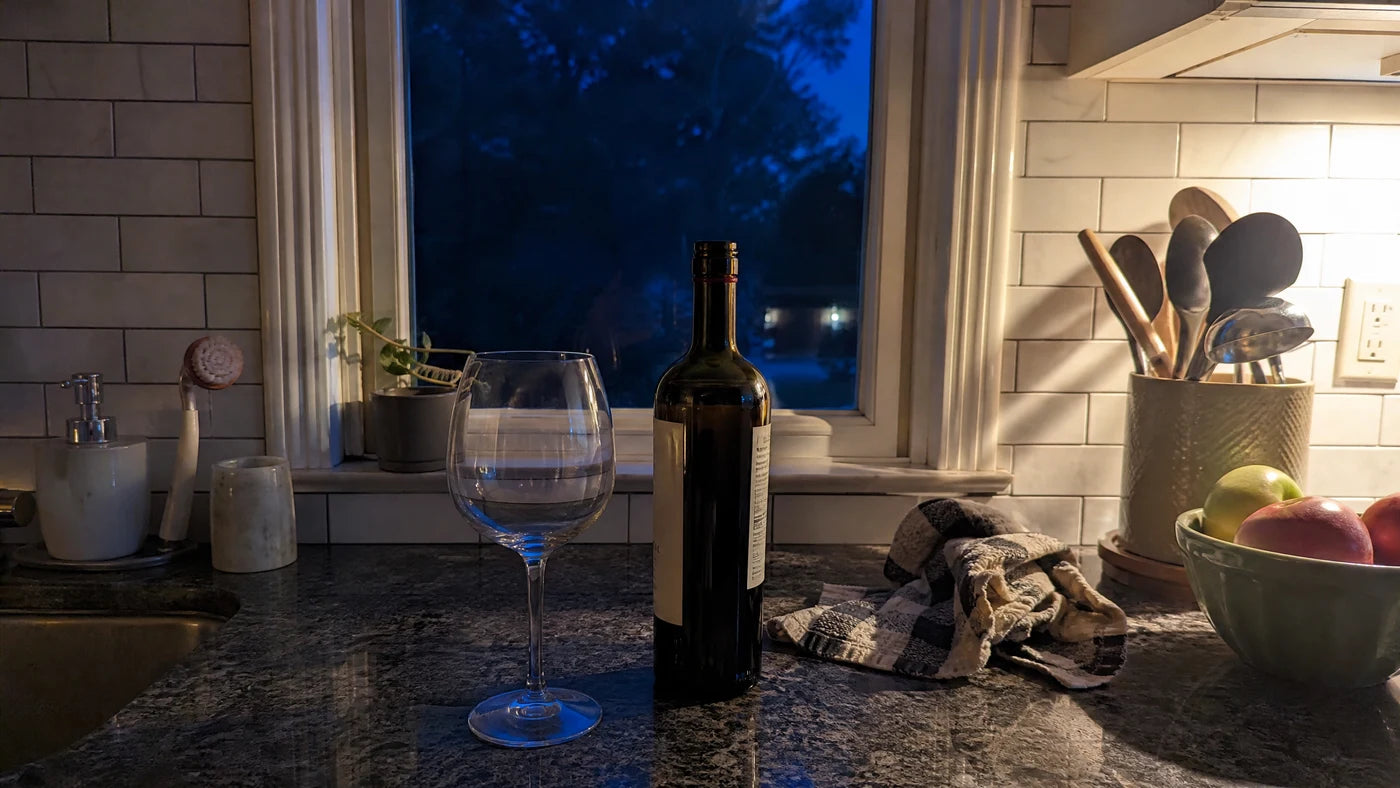 Empty wine glass and bottle on a dark kitchen counter just after dusk