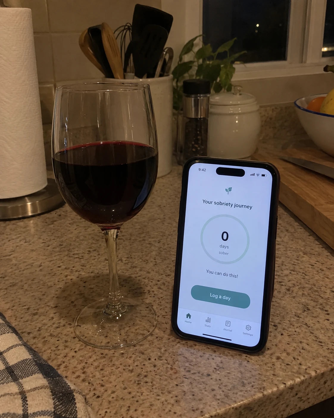 Phone showing a sobriety tracker app reset to zero days, sitting next to a full glass of red wine on a kitchen counter