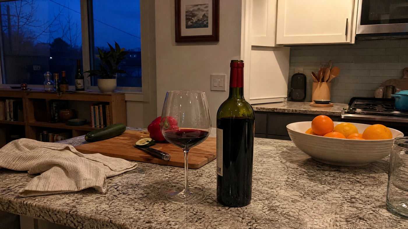 A wine glass and open bottle on a quiet kitchen counter in the early evening