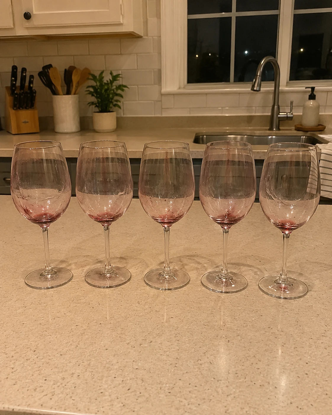 A row of empty wine glasses lined up on a kitchen counter, used night after night