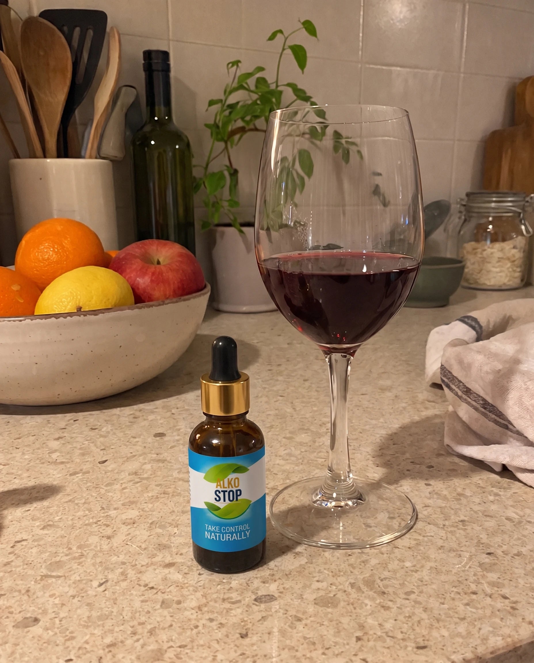 AlkoStop dropper bottle on a kitchen counter beside a glass of wine