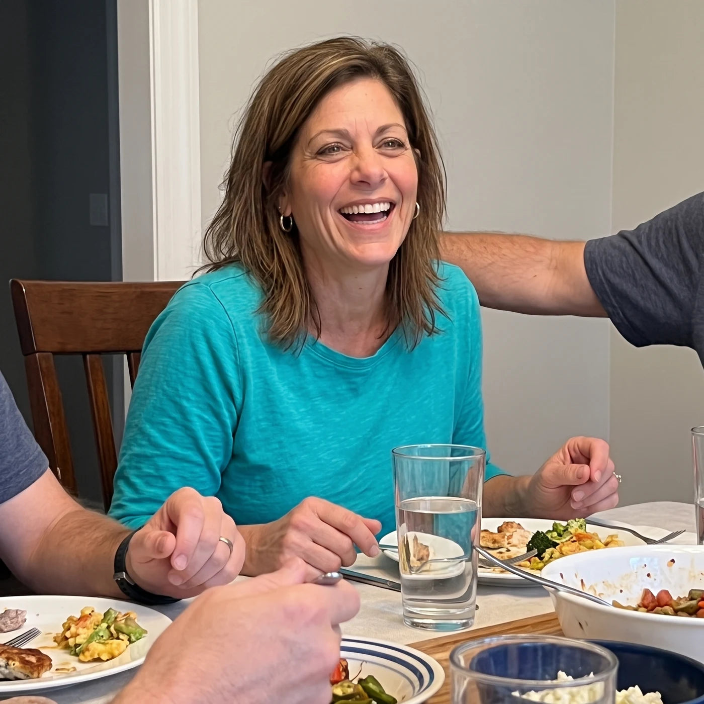 A woman laughing genuinely at a dinner table, a plain glass of water in front of her instead of wine