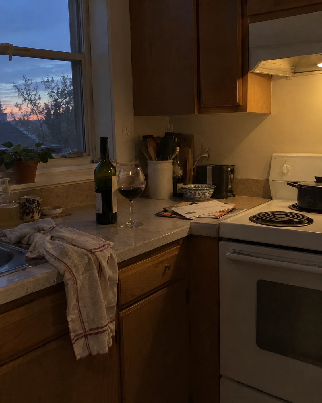 Kitchen counter at dusk with a bottle of wine and a poured glass, nobody in frame
