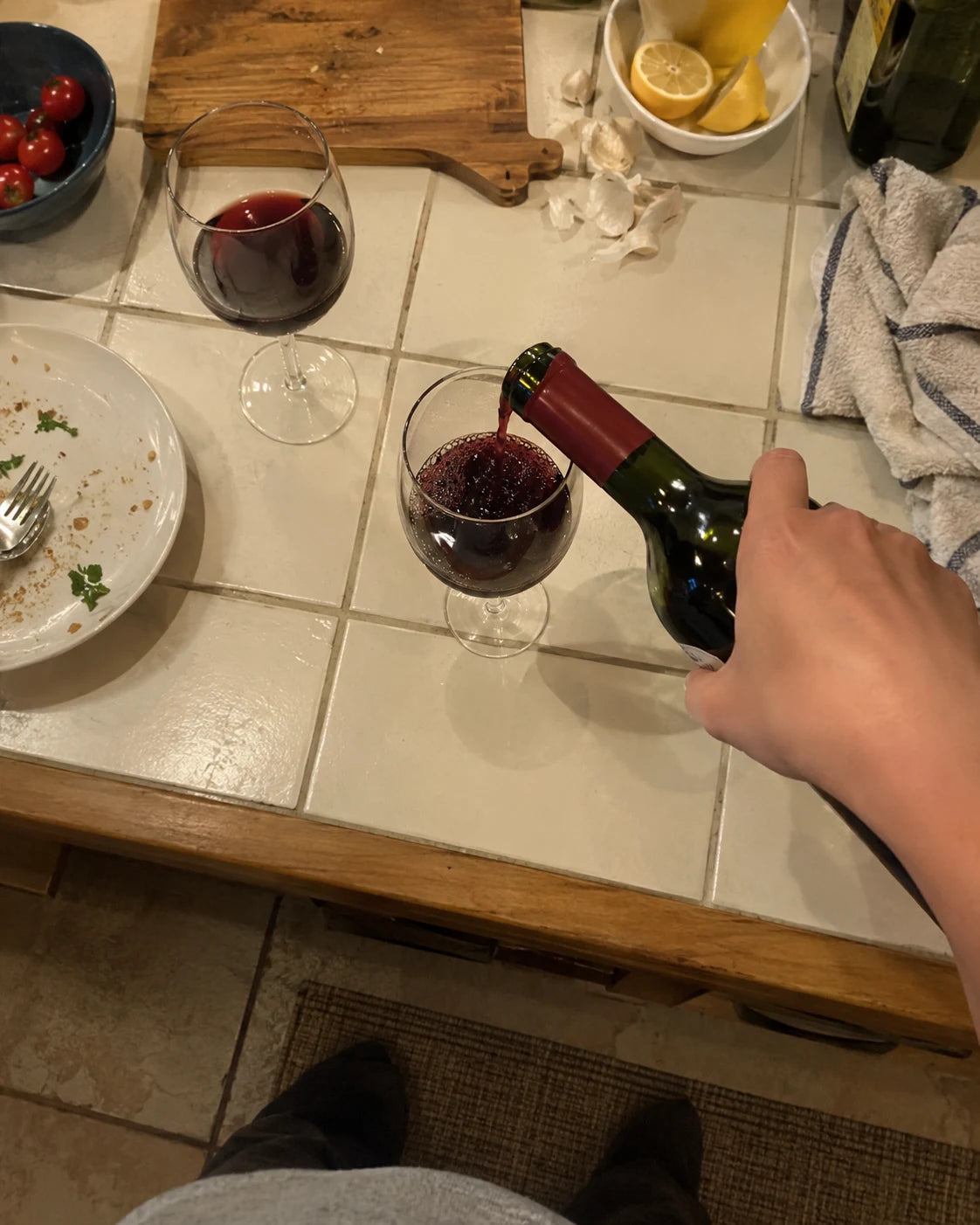 First-person view of a hand pouring a second glass of wine at night