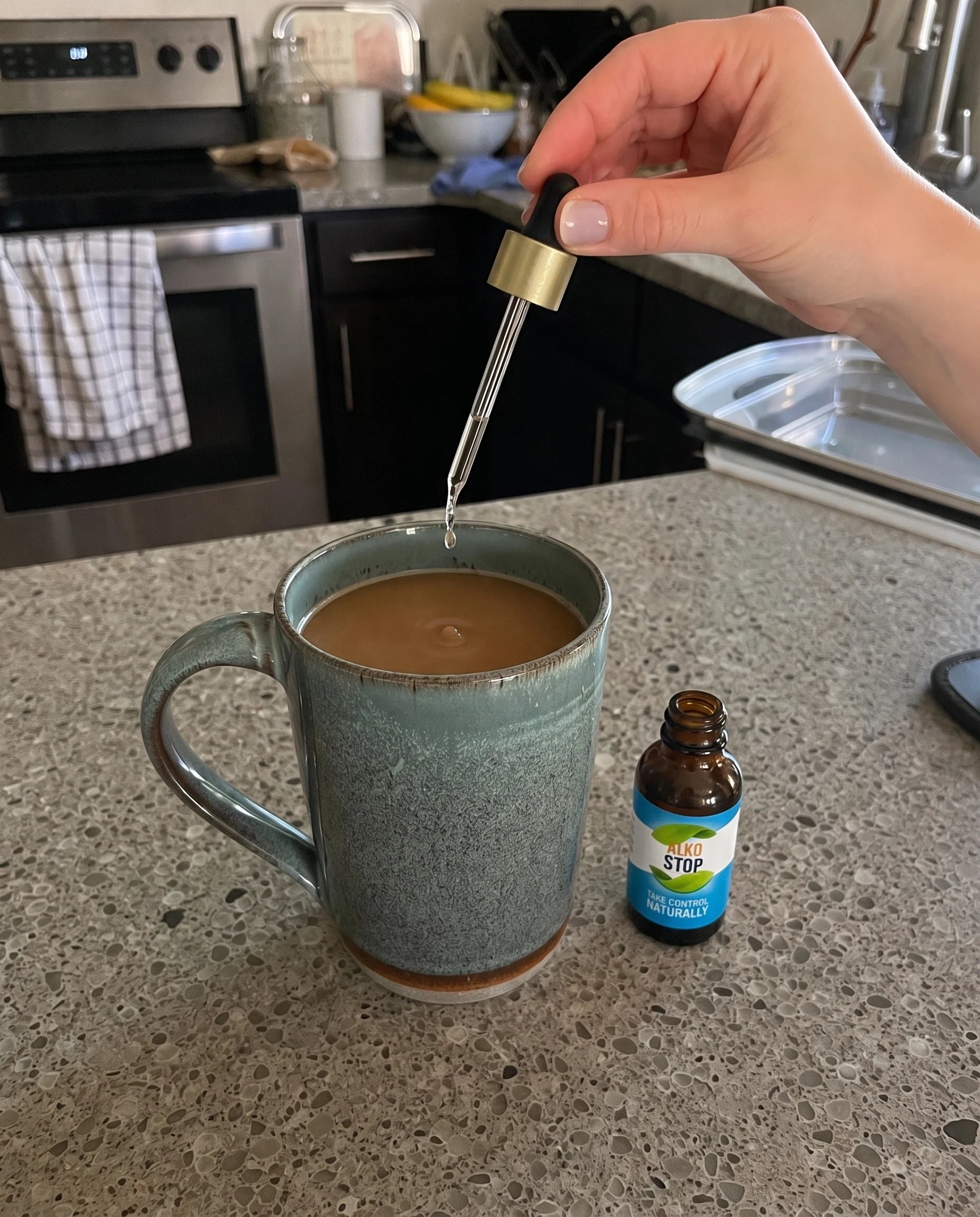 An open AlkoStop bottle resting on the counter while a hand holds the dropper centered above a cup of coffee