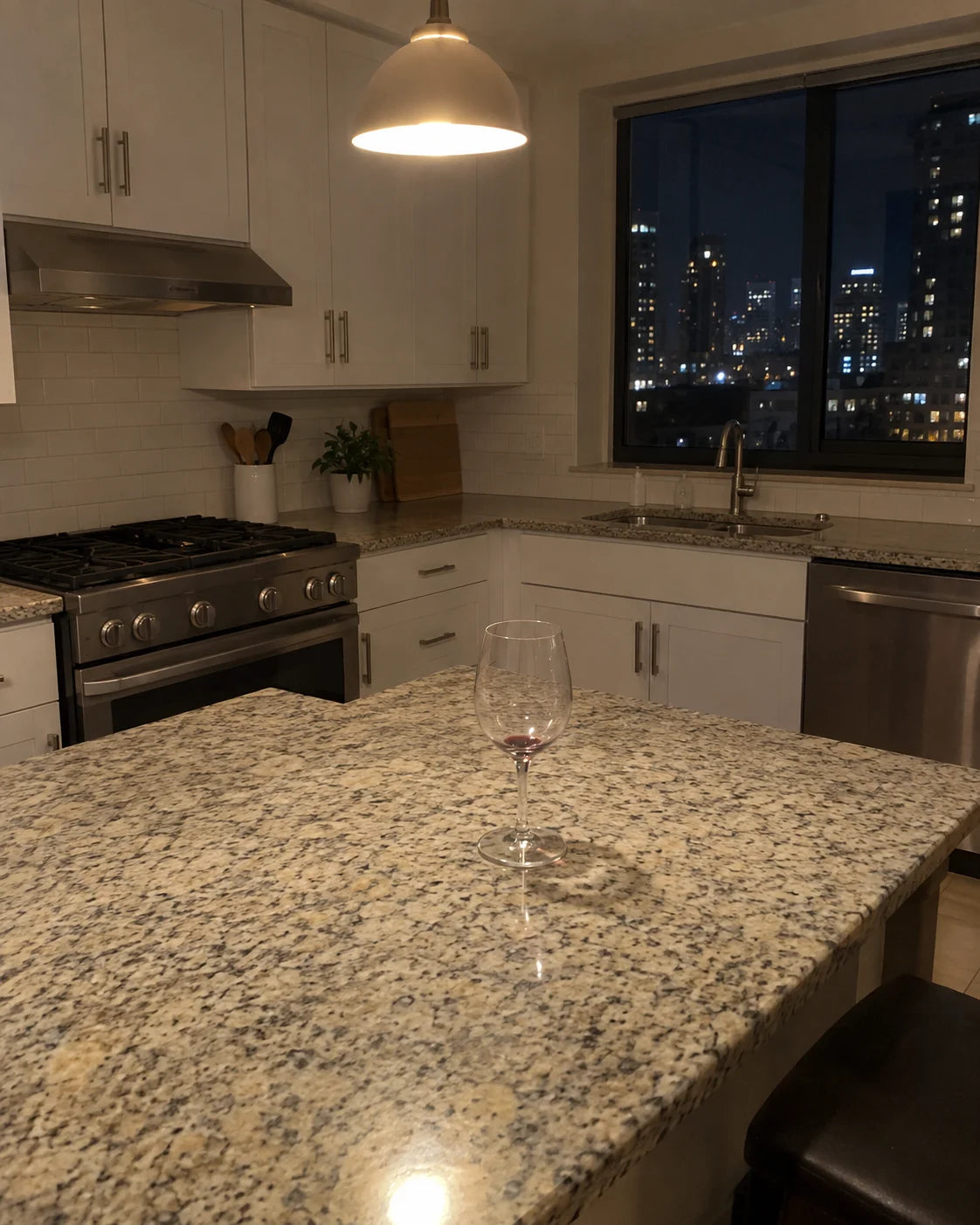 A single empty wine glass alone on a dim kitchen counter at night