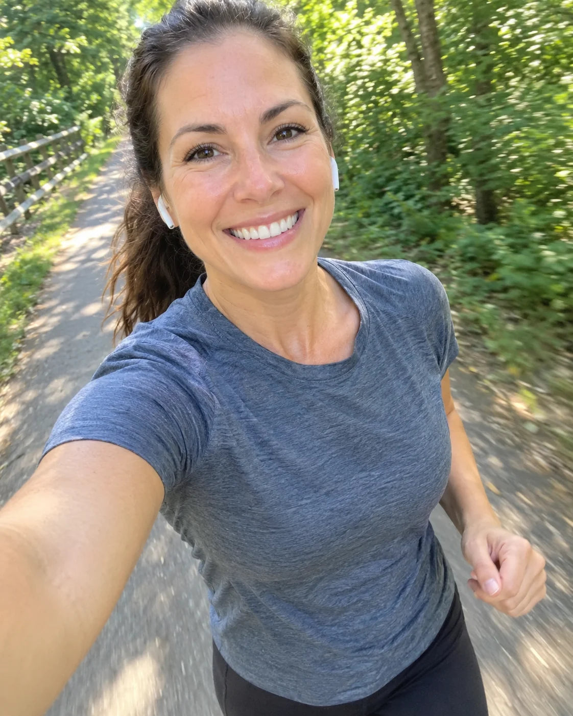 A smiling woman taking a happy selfie while jogging outdoors on a sunny trail