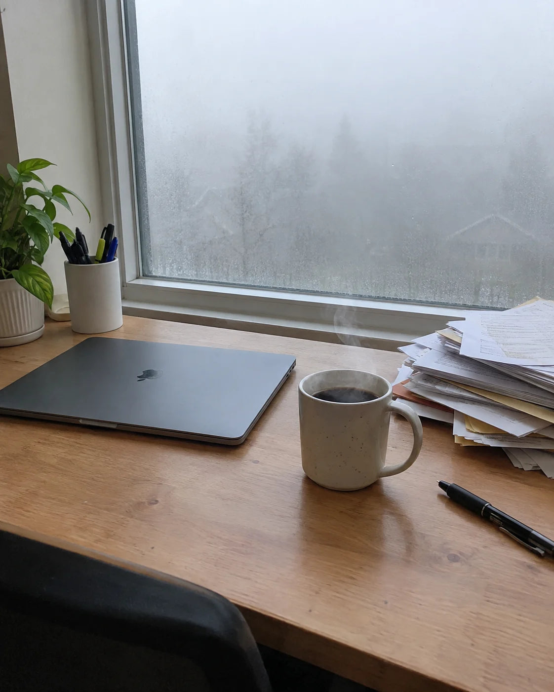 Desk with coffee and a laptop, a foggy morning visible through the window
