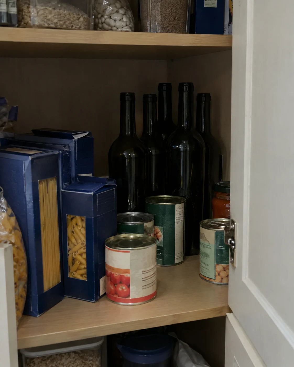 Empty wine bottles tucked behind pantry goods in a kitchen cabinet