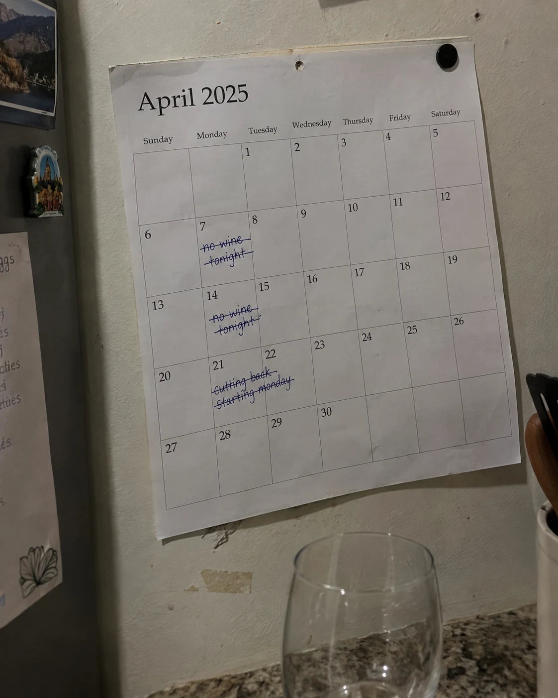 Kitchen wall calendar with handwritten no wine tonight notes crossed out, empty wine glass below