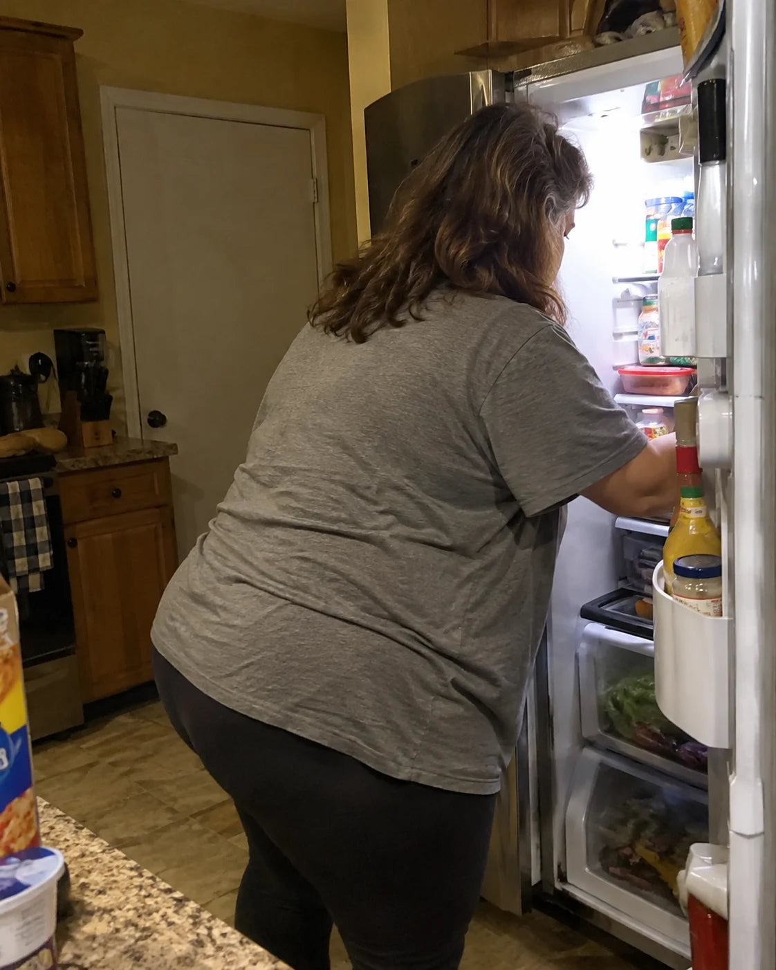 Woman glancing back from an open refrigerator late at night