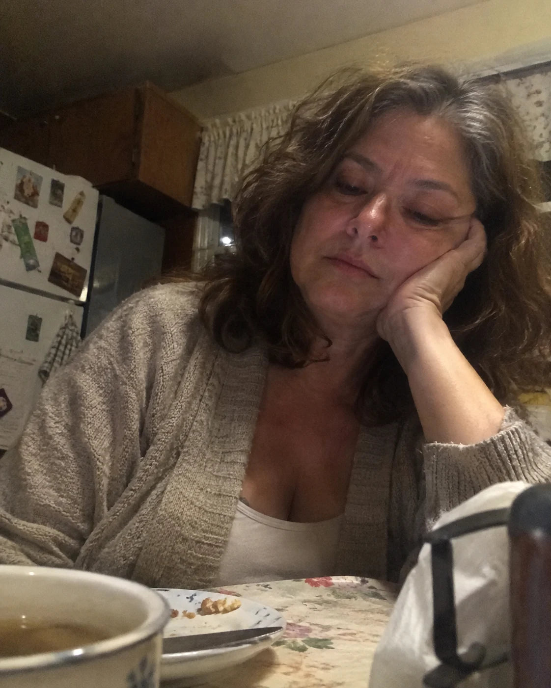 Woman sitting alone at her kitchen table late at night, head resting on her hand