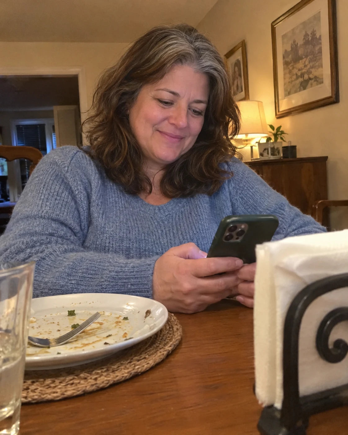 Woman relaxed at the dinner table, plate pushed aside, looking at her phone