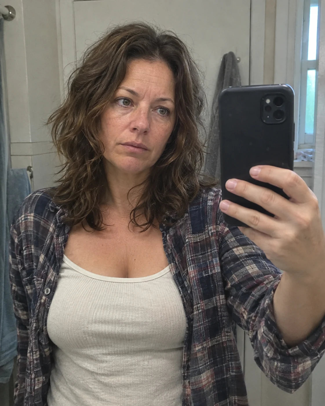 Woman taking a tired bathroom mirror selfie in the morning, phone visible in hand