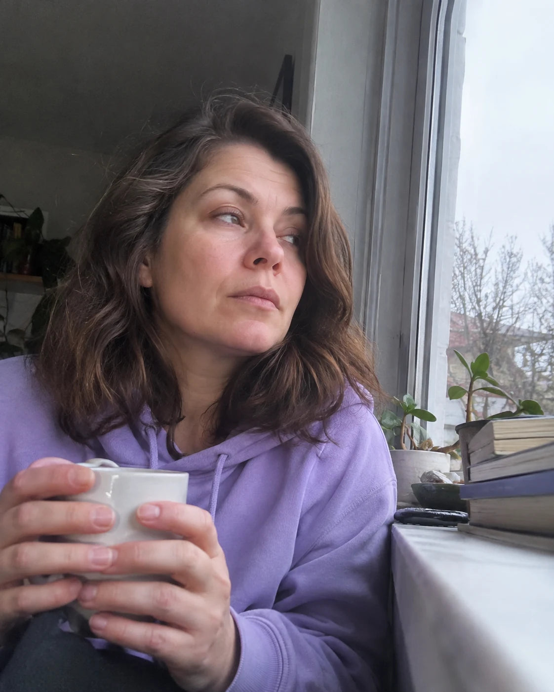 Woman sitting by a window in soft daylight holding a mug of tea, no wine in sight