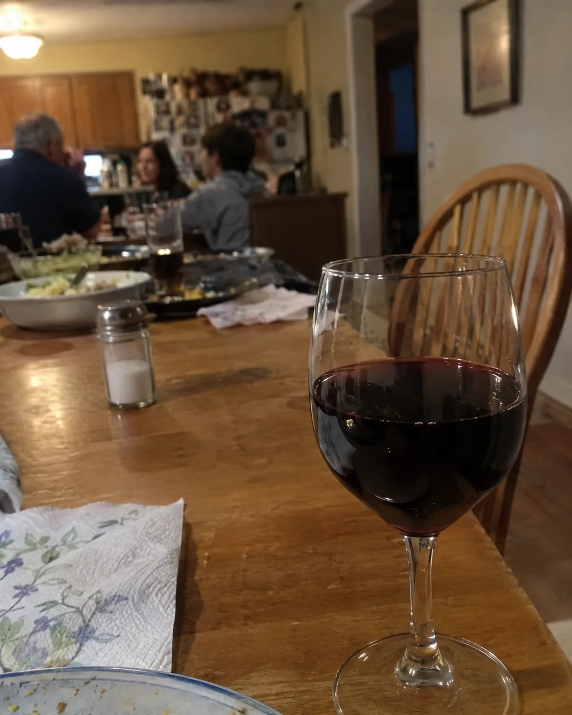 A wine glass in sharp focus on a family dinner table with blurred family members in the background