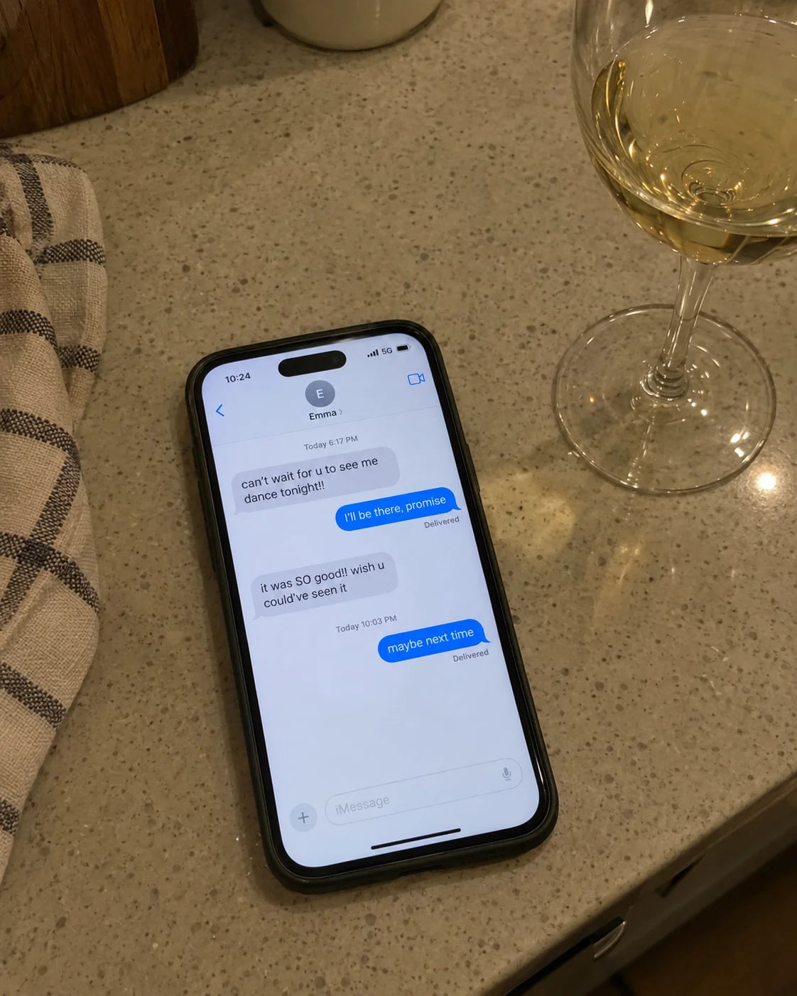 A phone on a kitchen counter showing a text thread from Kids reading maybe next time, next to a wine glass