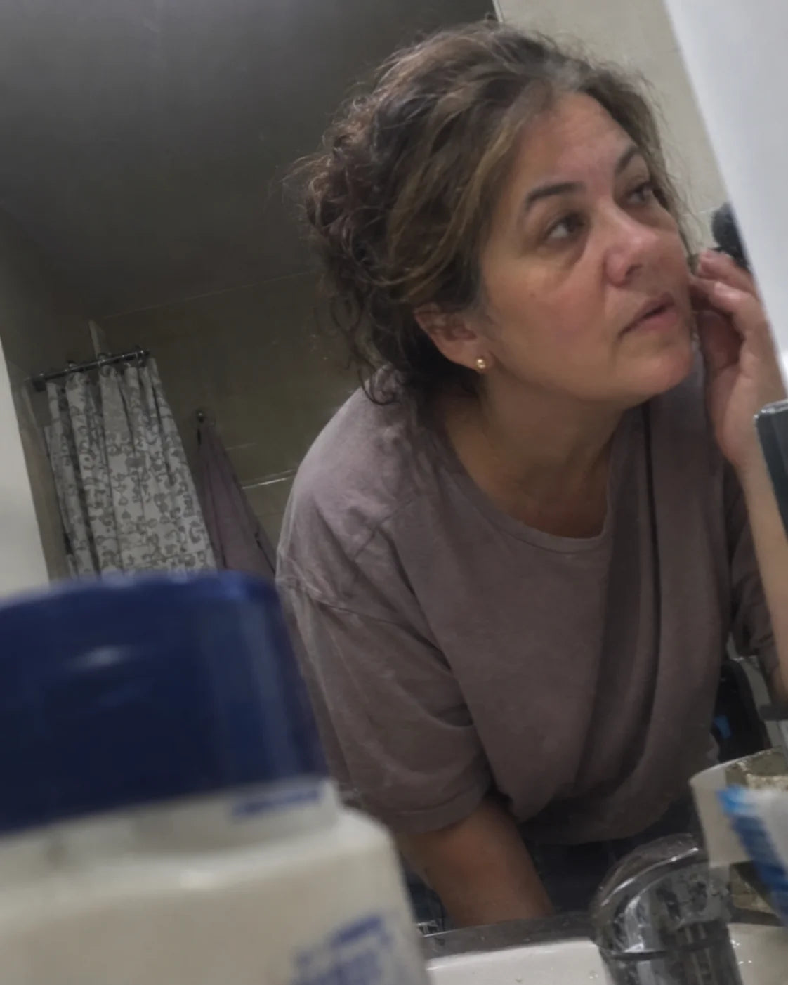 A tired woman examining her reflection in a bathroom mirror at night