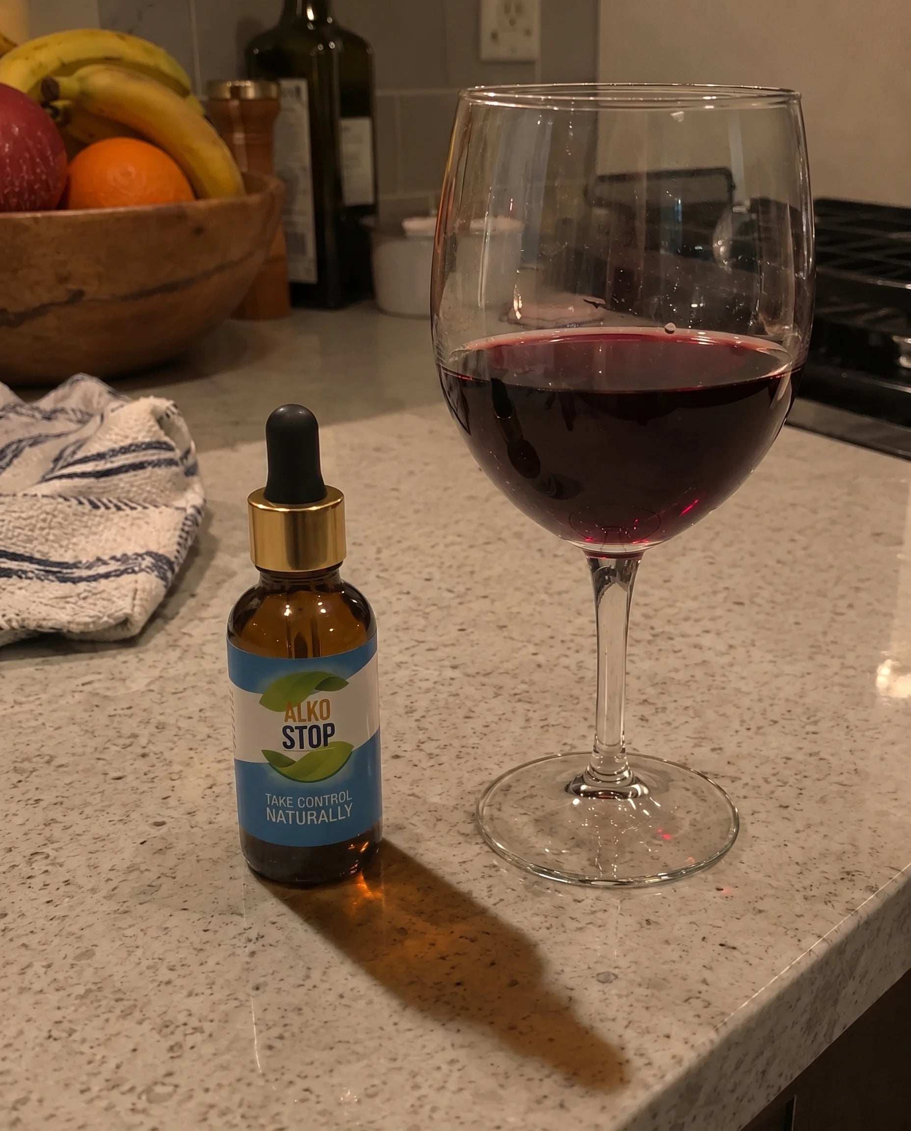 The AlkoStop dropper bottle sitting next to a full wine glass on a kitchen counter