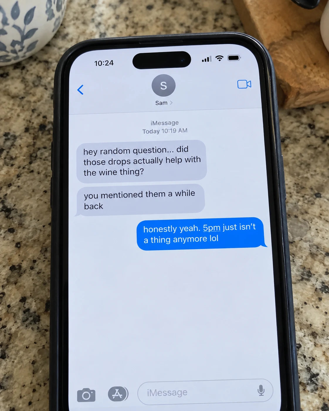 A phone screen on a kitchen counter showing a text message about natural drops helping with wine cravings
