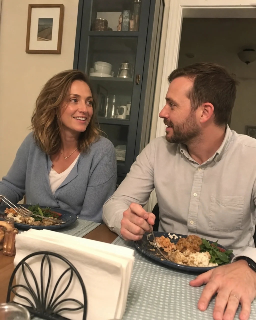 A woman and her husband smiling and talking over dinner at home