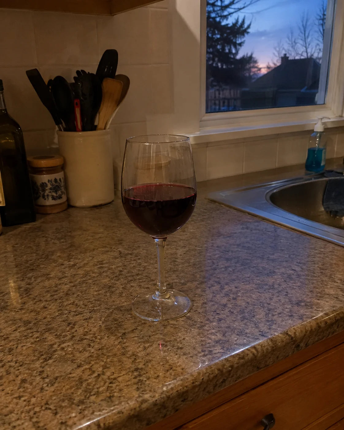 A single glass of wine alone on a kitchen counter at dusk