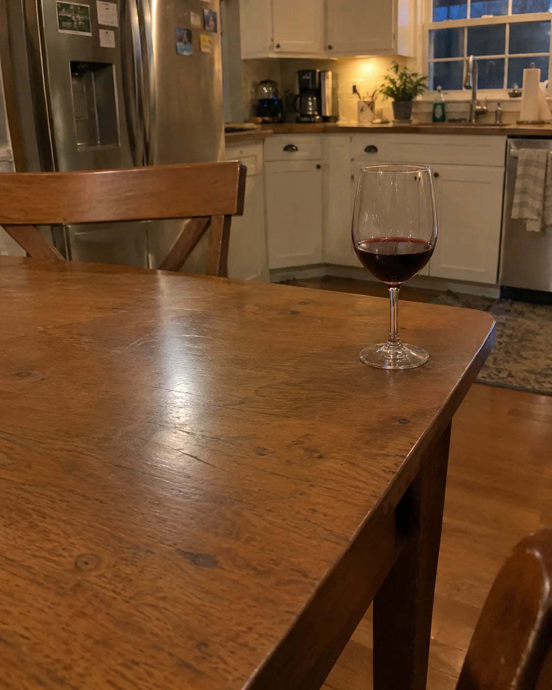 A glass of wine pushed to the edge of a dining table, mostly untouched