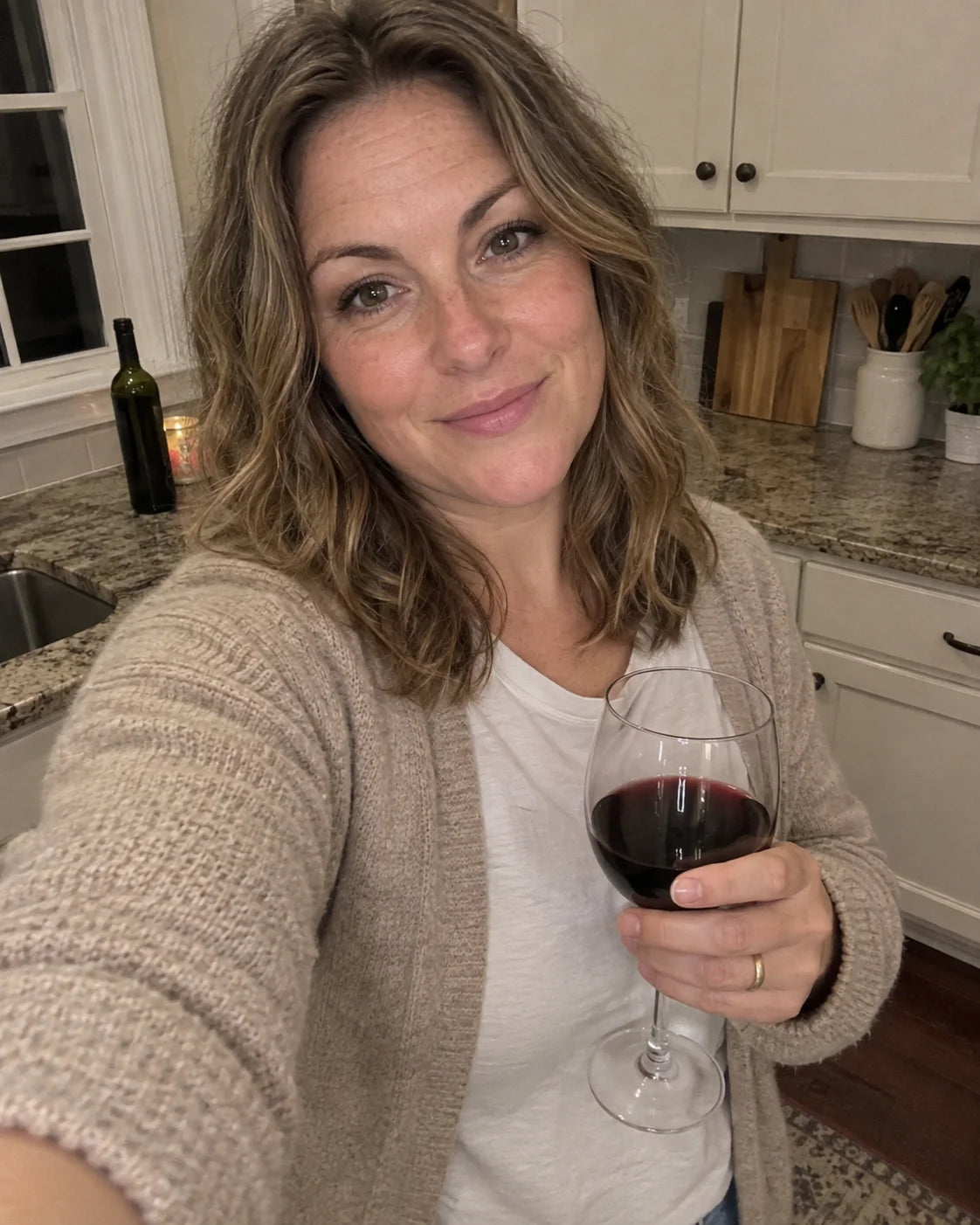 Woman pouring a glass of red wine at the kitchen counter in the evening
