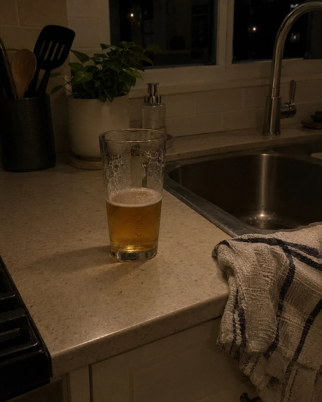 Half-finished glass of beer left on a kitchen counter at night