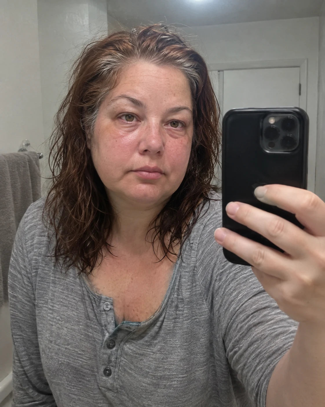 A woman taking a tired, puffy-faced mirror selfie in her bathroom