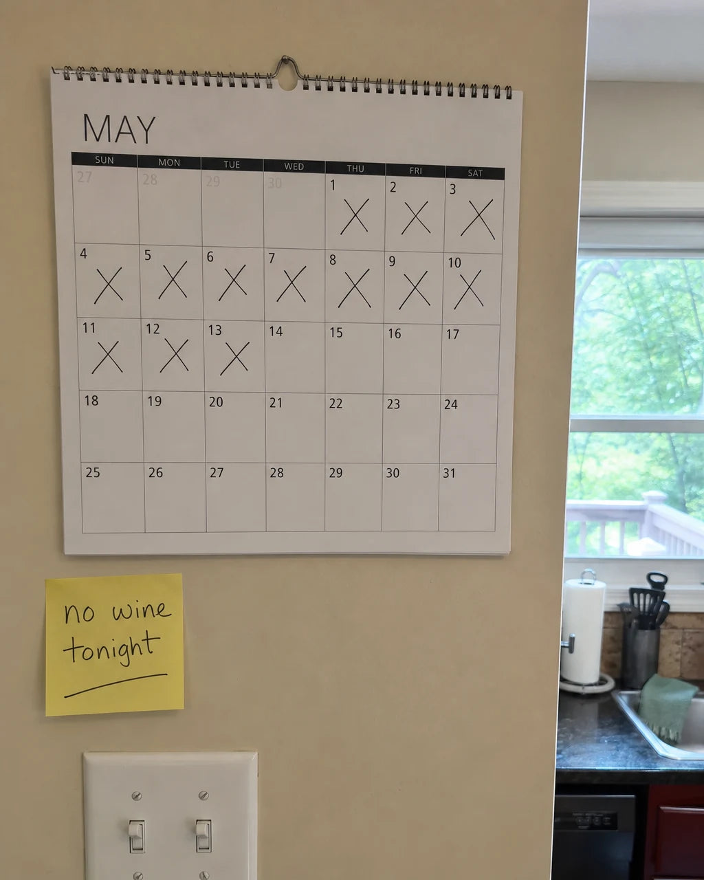 A kitchen calendar with crossed out days under a handwritten note that says no wine tonight