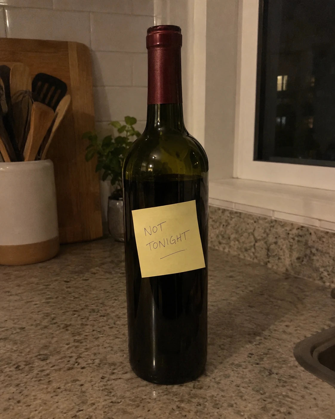 A sticky note reading not tonight stuck directly onto a wine bottle on a kitchen counter