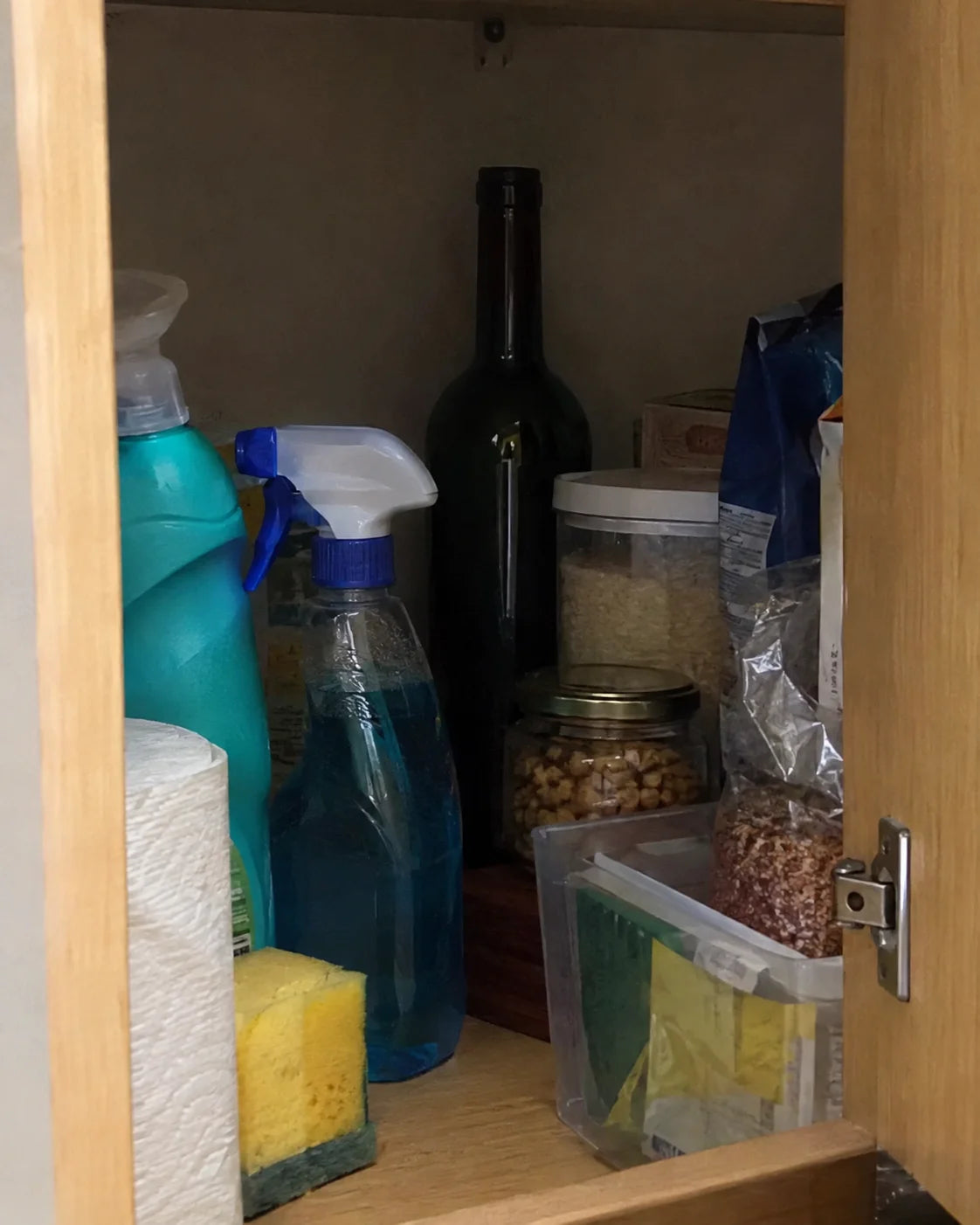 An empty wine bottle tucked behind cleaning supplies at the back of a kitchen cabinet
