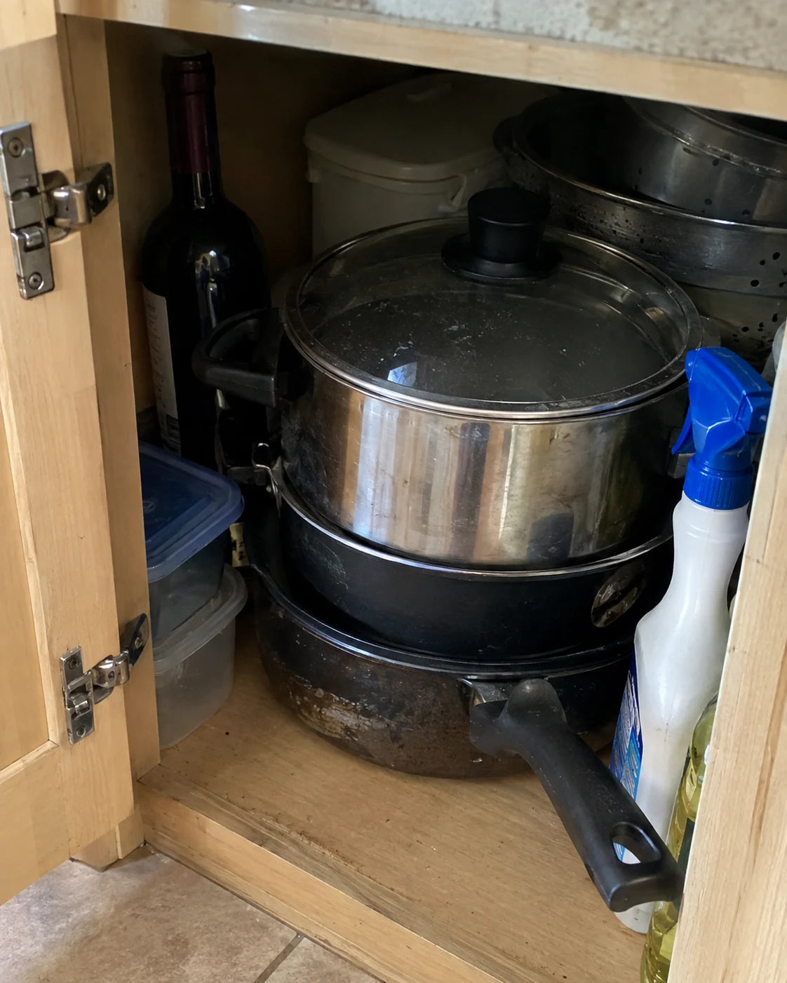 A wine bottle hidden behind pots in a kitchen cabinet