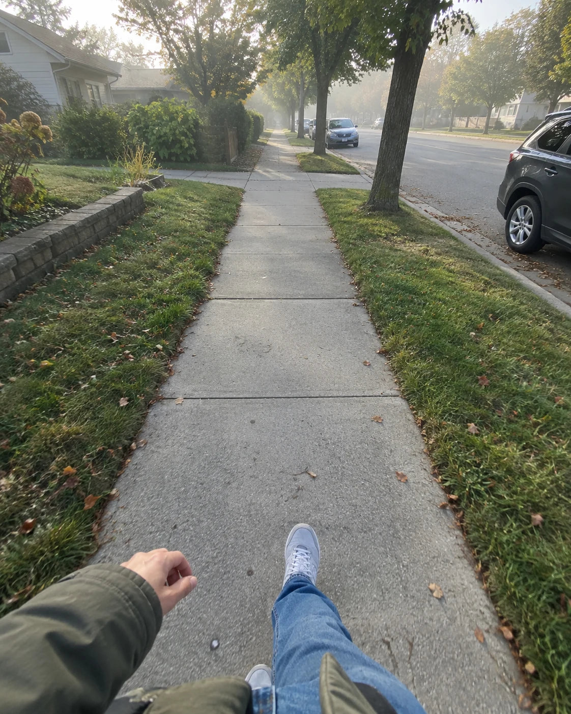 First-person view walking along a quiet residential sidewalk in soft morning light