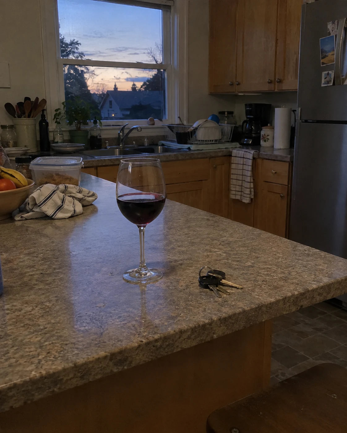 A glass of wine already poured on a kitchen counter next to keys and a phone at dusk