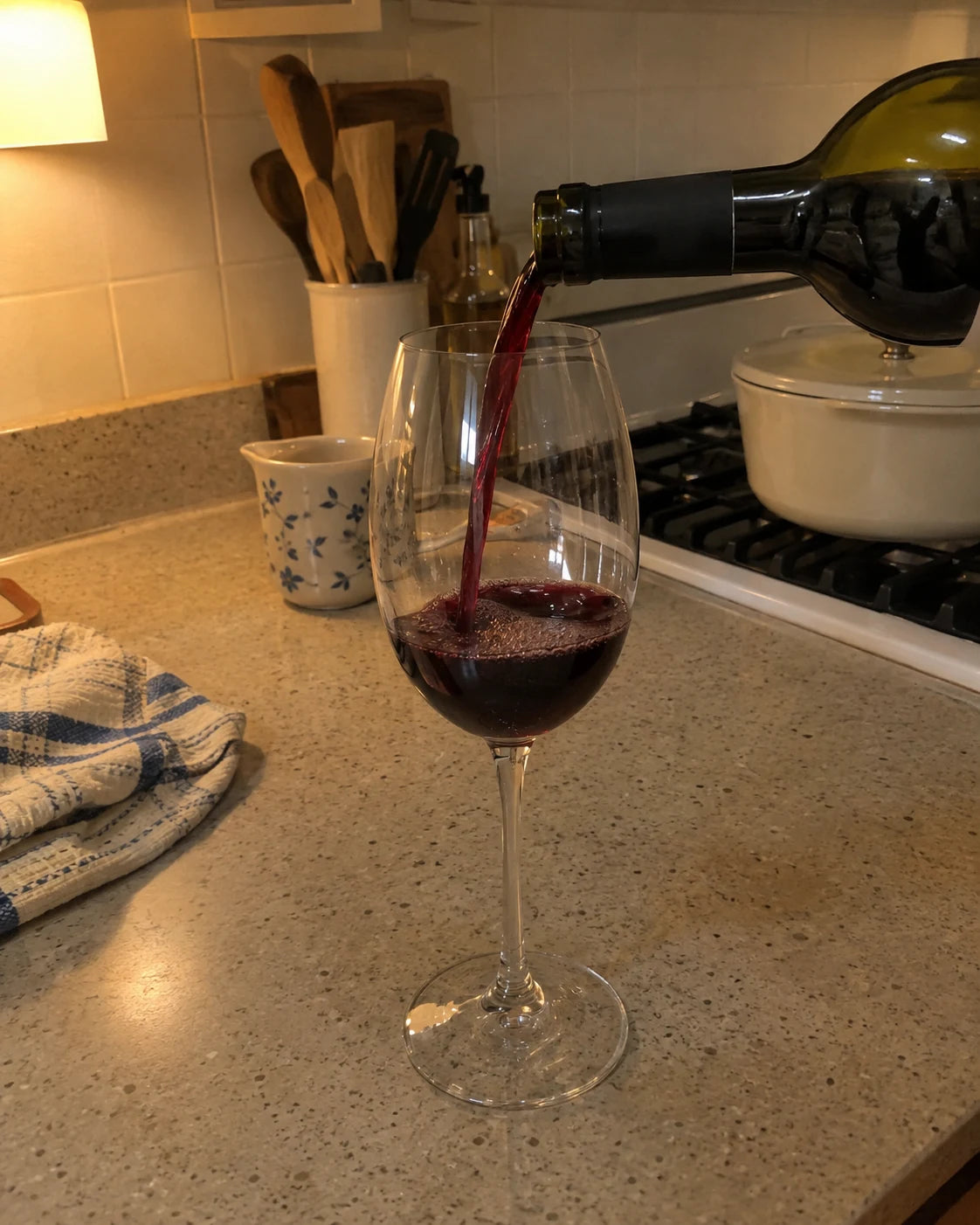 Red wine being poured into a glass on a kitchen counter in the evening