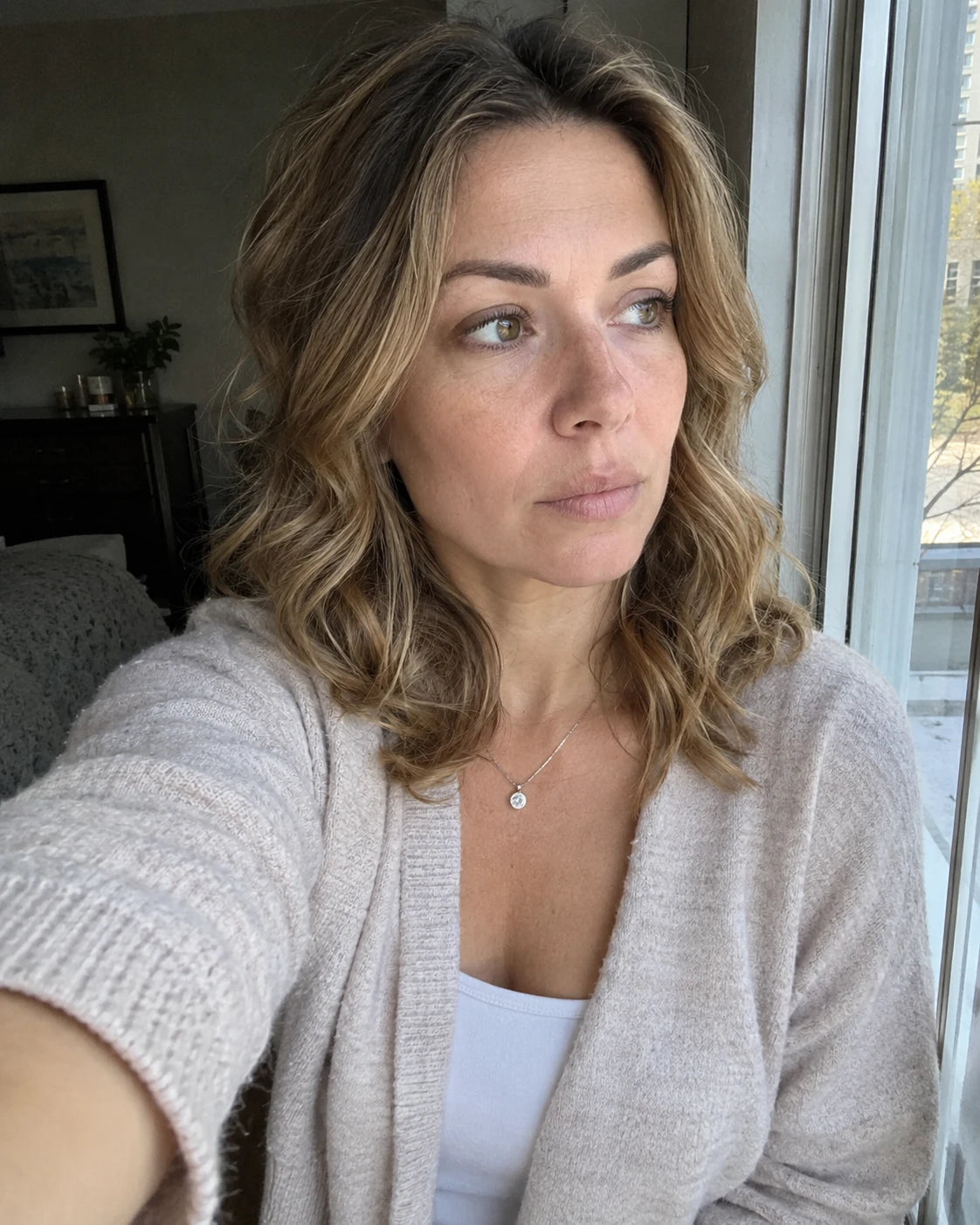A woman taking a quiet, tired selfie by a window in late afternoon light