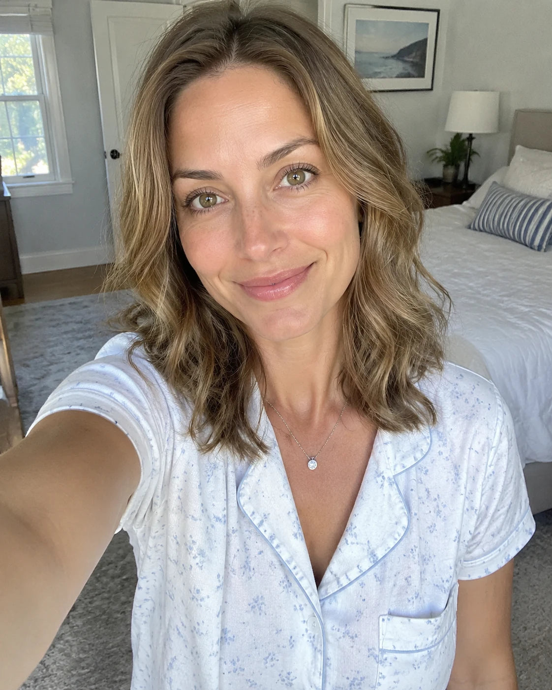 A woman taking a calm, well-rested selfie in a bright bedroom in the morning