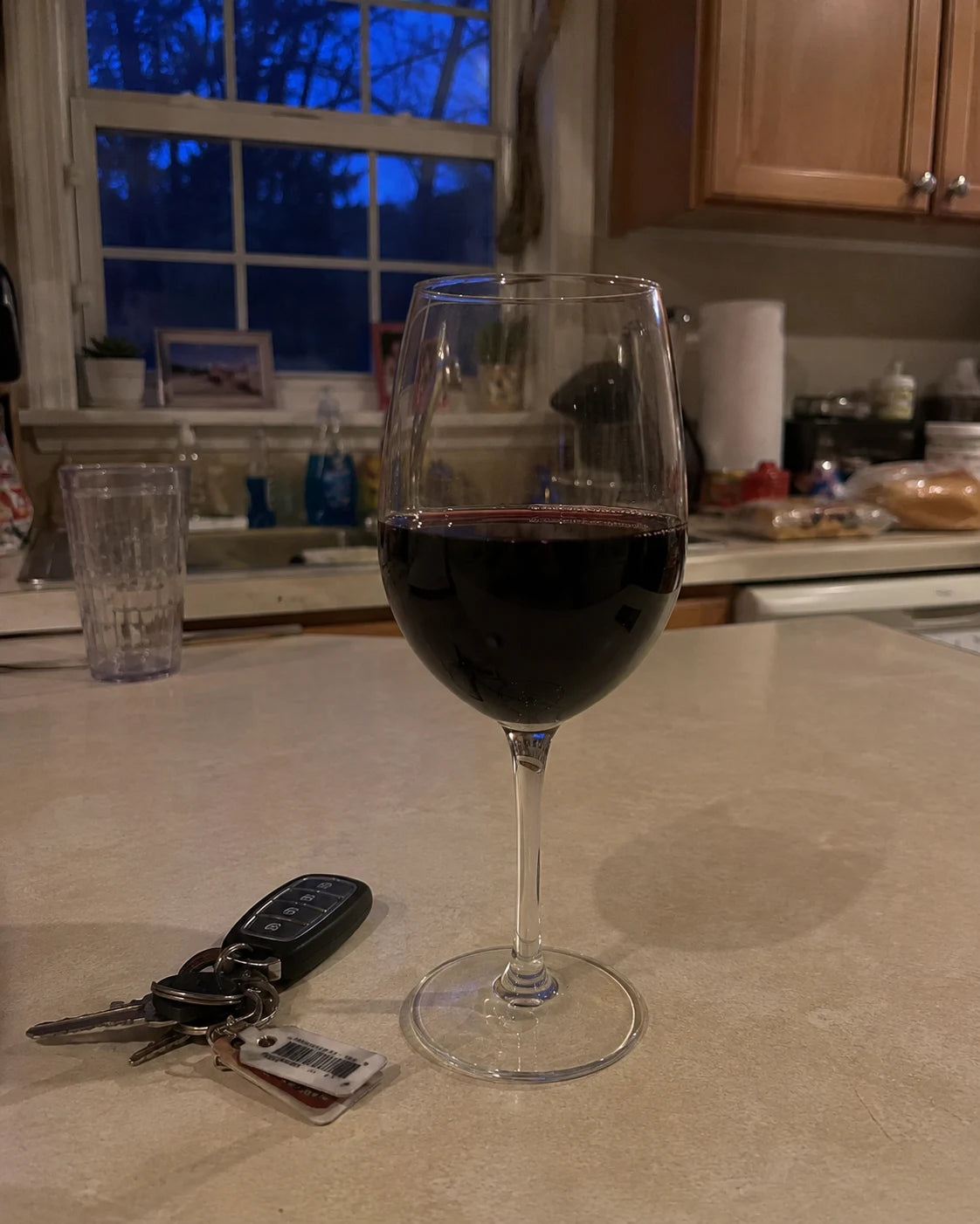 A full glass of wine already poured on a kitchen counter next to keys and a phone at dusk