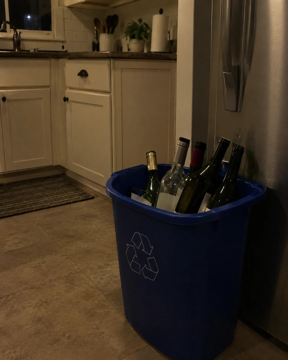 A recycling bin full of empty wine bottles in a dim kitchen at night, showing a repeated nightly pattern