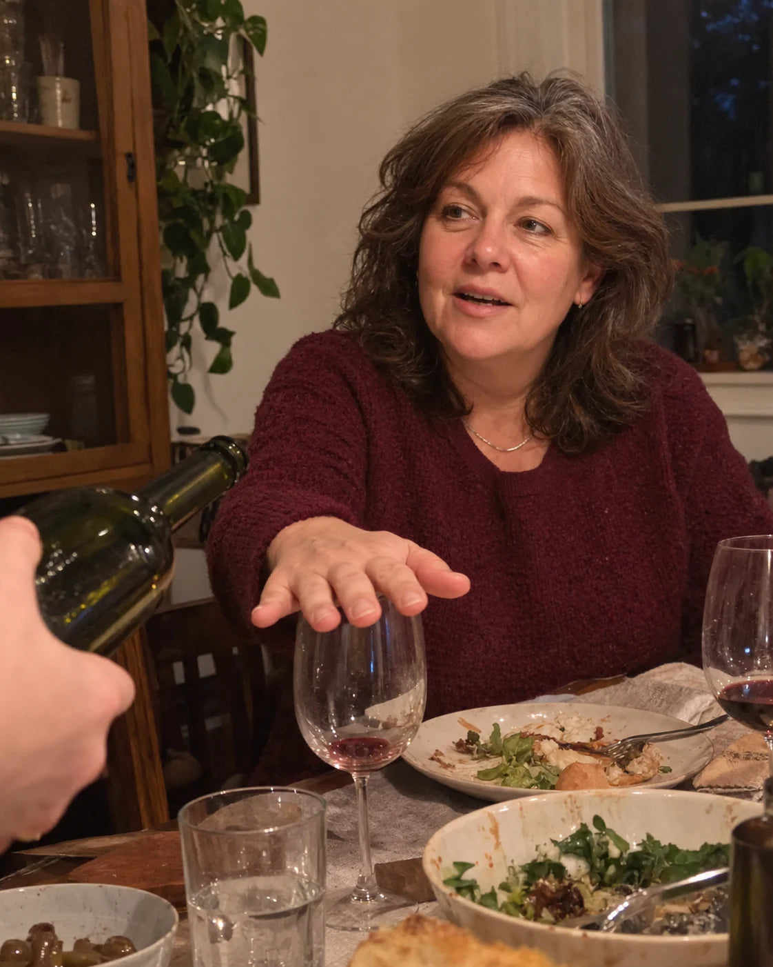 Woman at a dinner table with her hand resting over her wine glass as a friend reaches to refill it