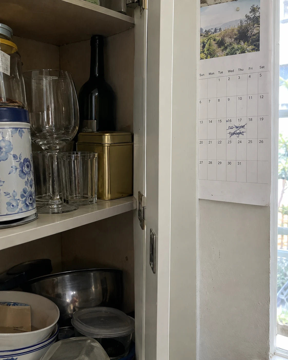 A wine bottle pushed to the back of a kitchen cabinet next to a calendar page with no wine tonight crossed out