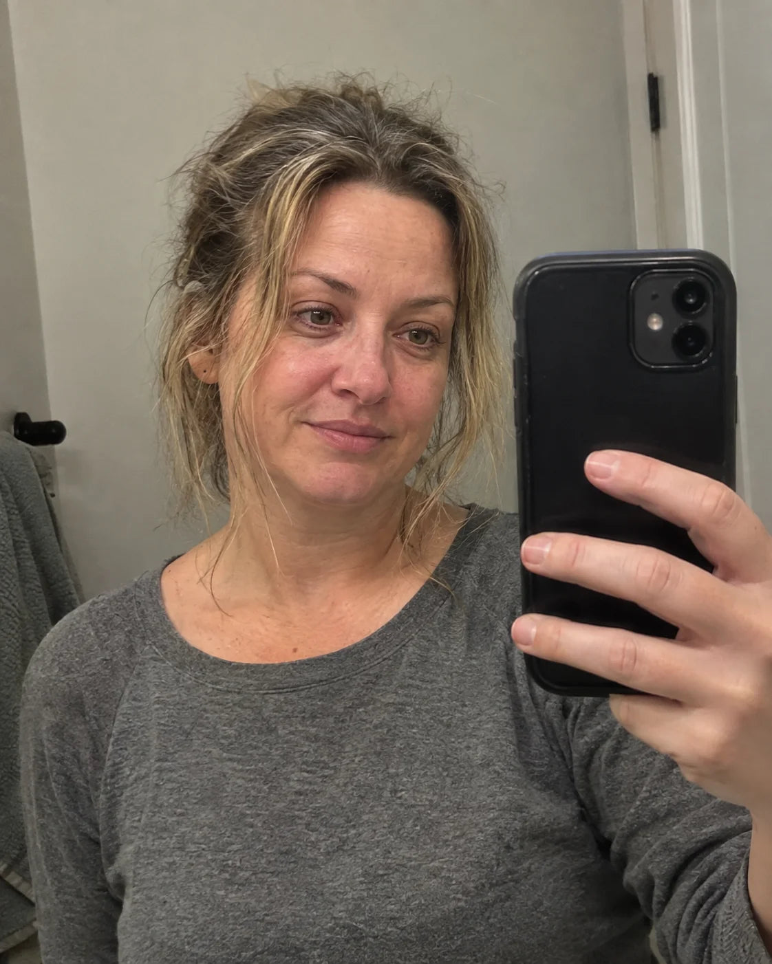 A tired woman looking at her puffy reflection in a bathroom mirror in the morning