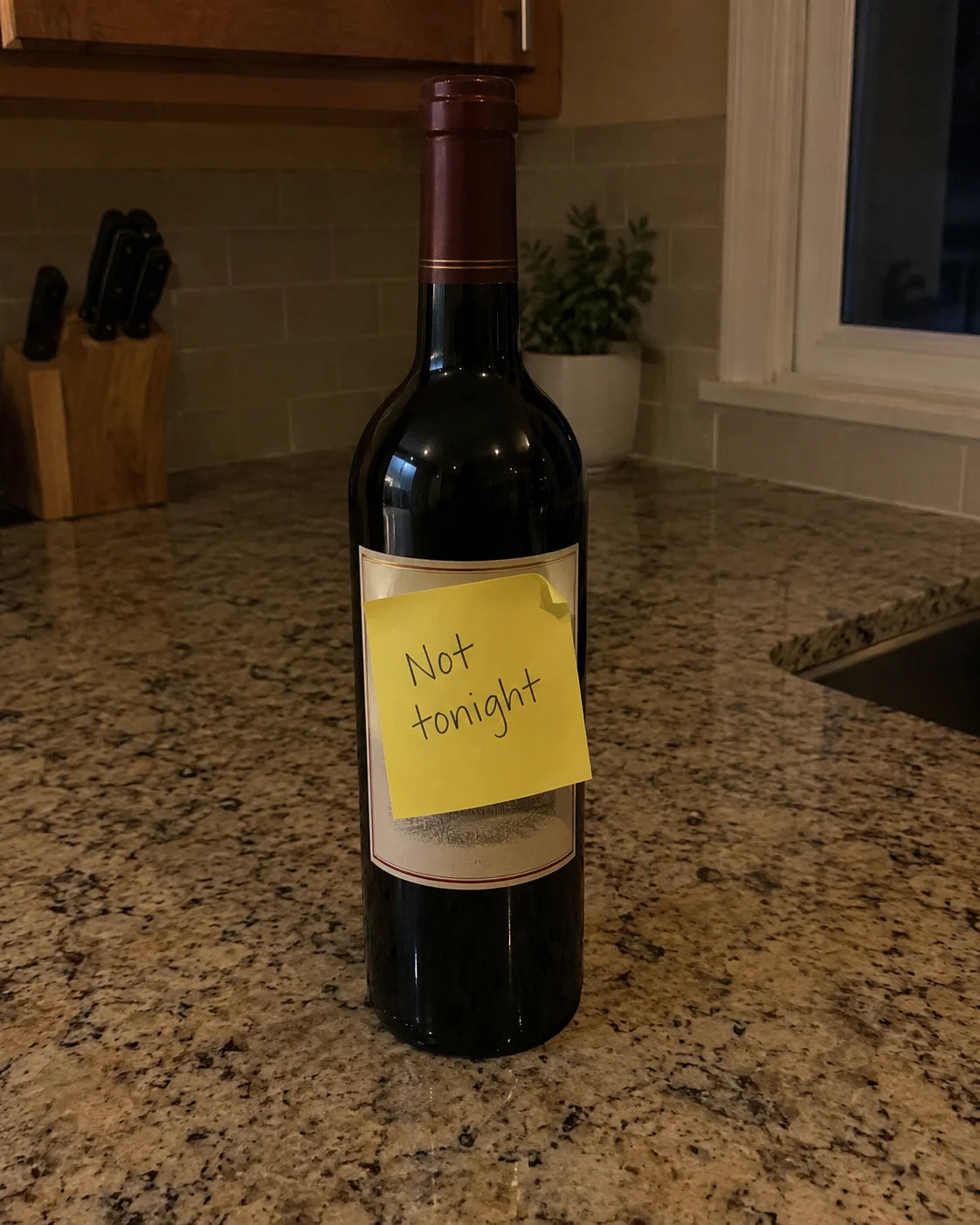 A sticky note reading not tonight stuck directly onto a wine bottle on a kitchen counter