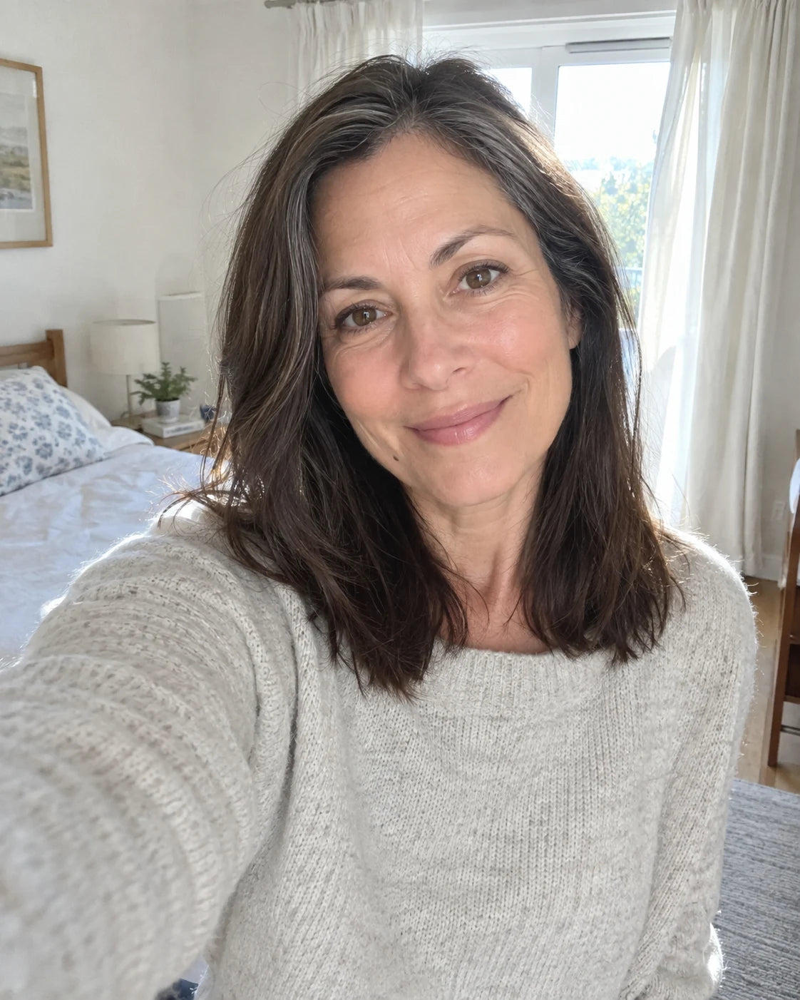 A woman taking a calm, well-rested selfie in a bright bedroom in the morning