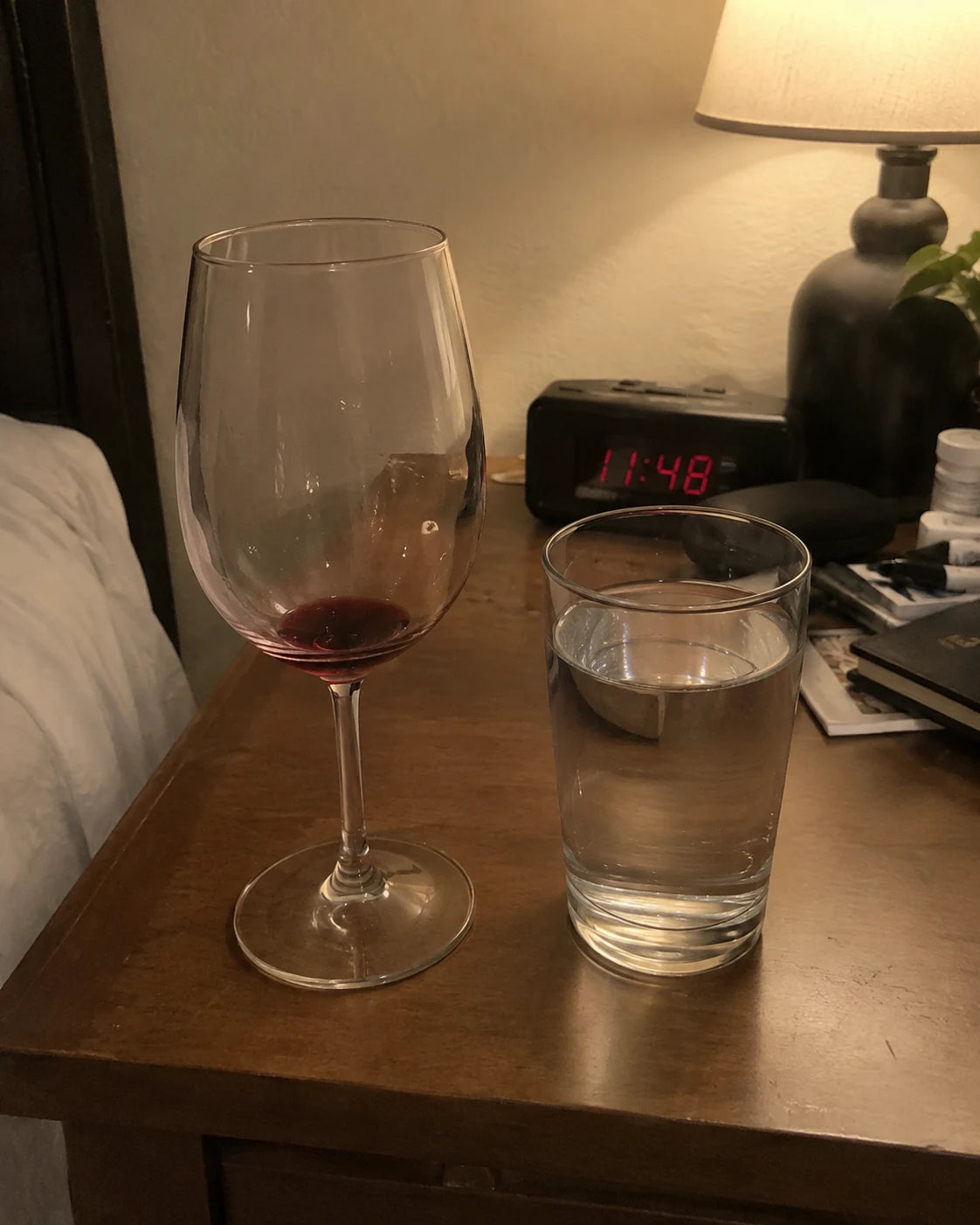 An empty wine glass next to a full glass of water on a nightstand at night