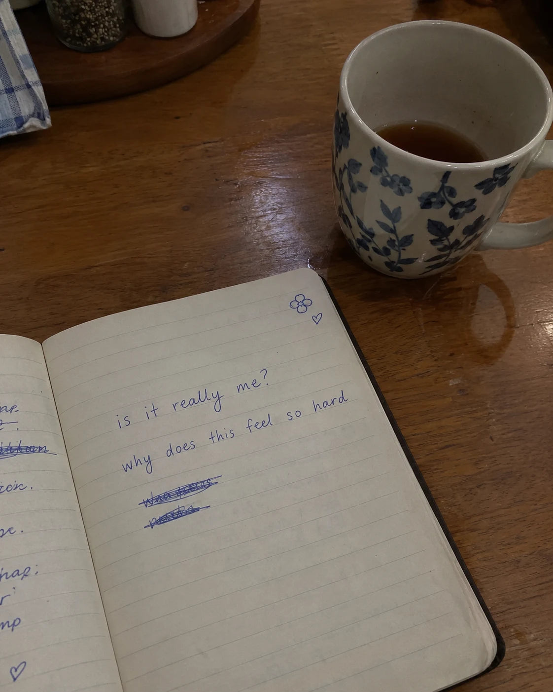 A handwritten journal page reading 'is it really me? why does this feel so hard' next to a cup of tea gone cold