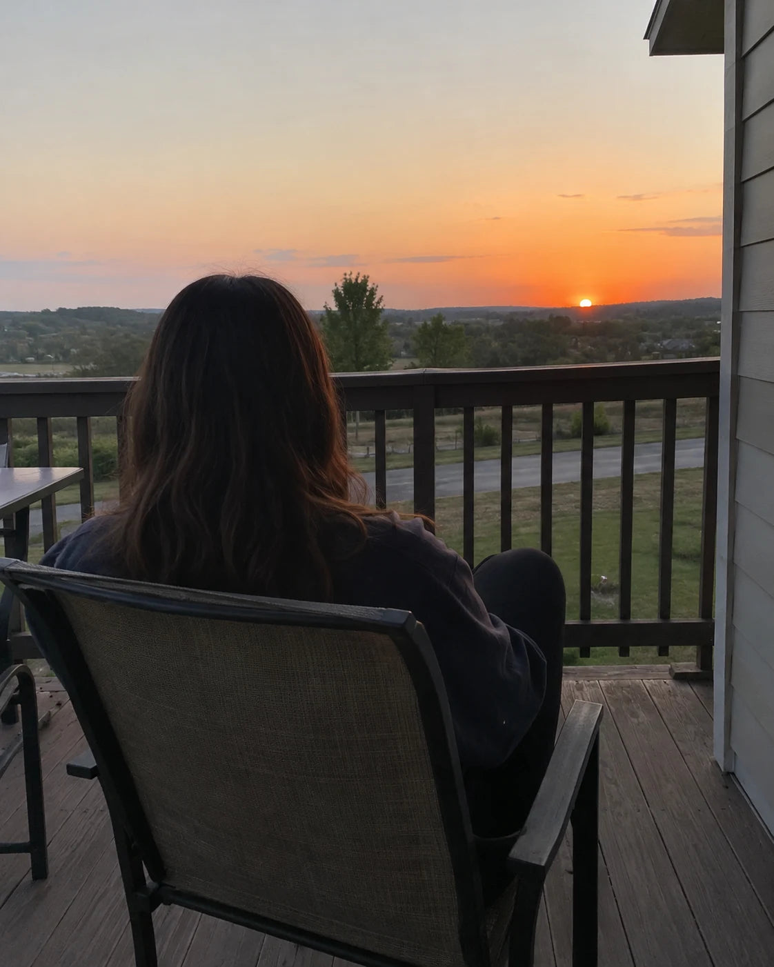 A woman seen from behind, relaxed on a porch chair at sunset, calm evening scene