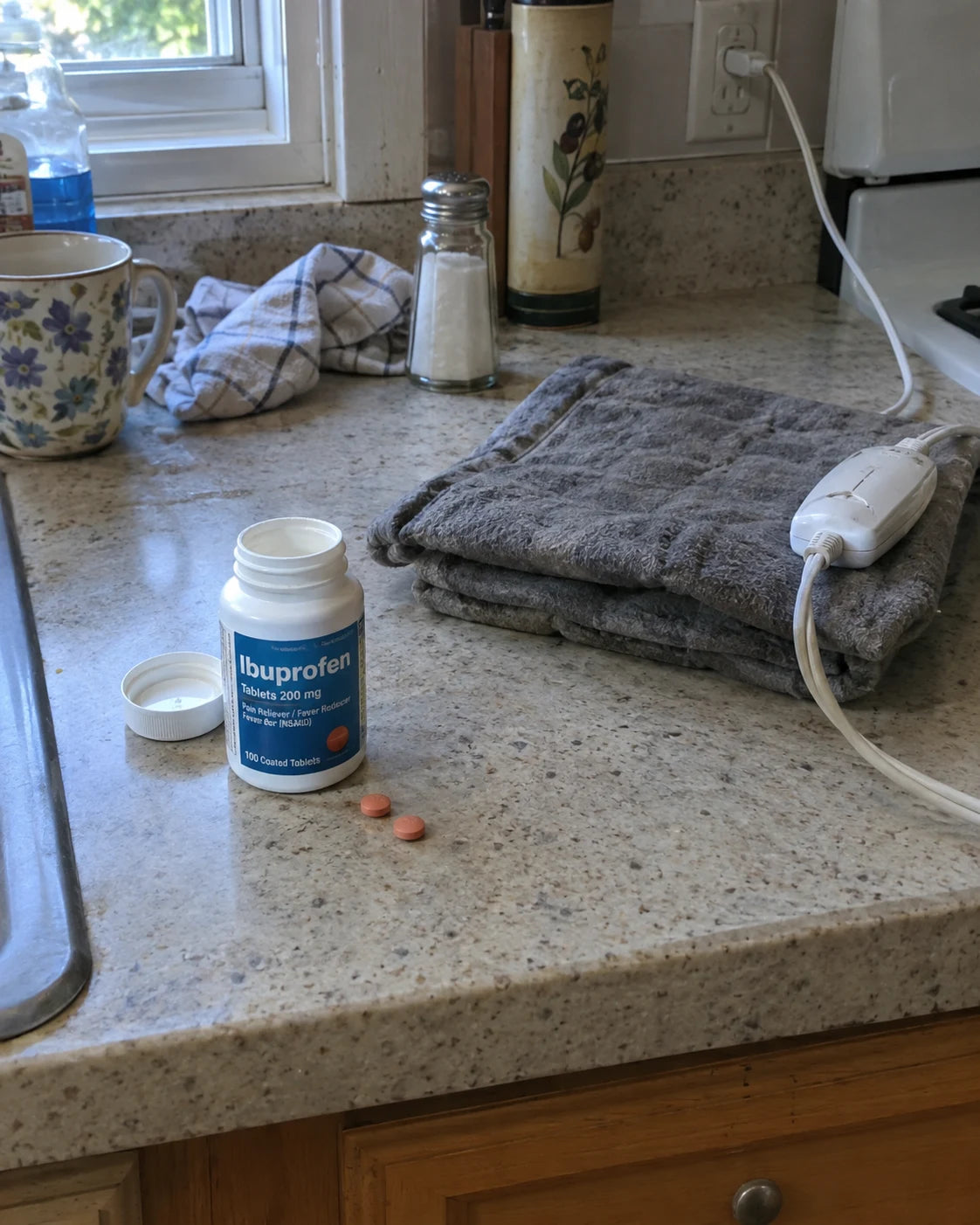 Ibuprofen bottle and heating pad on a kitchen counter